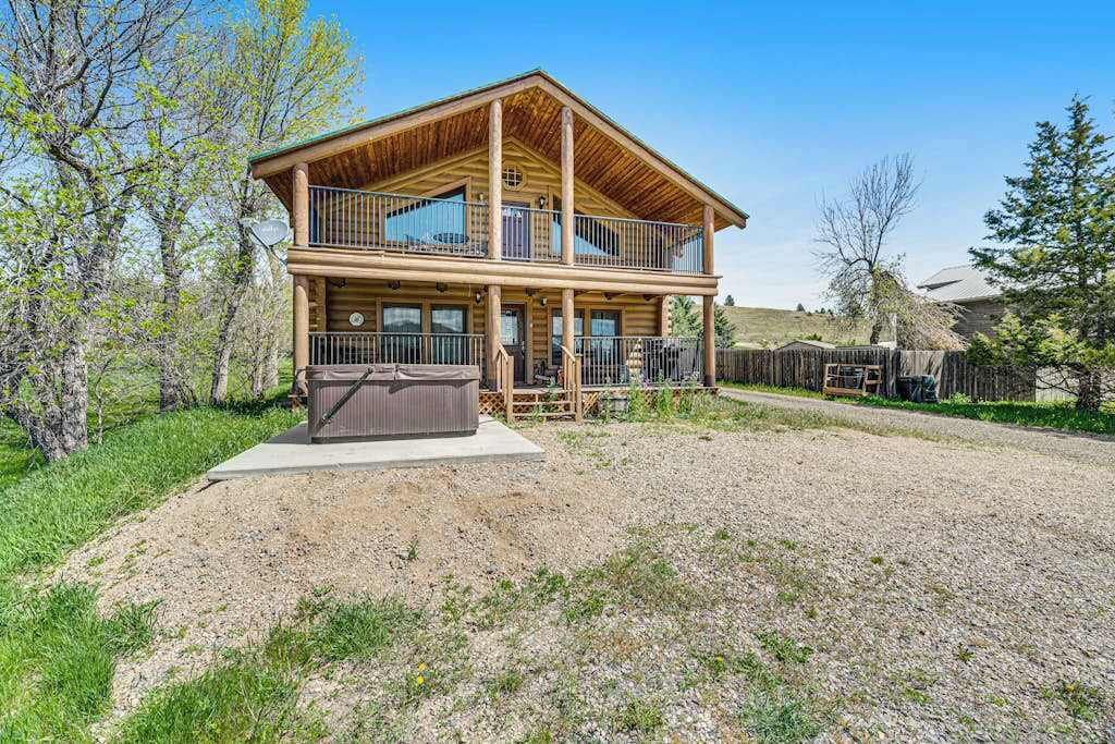 Une cabane en rondins à deux étages, dotée d’un balcon, d’un jacuzzi et d’une allée en gravier.
