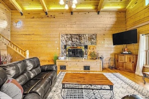 A wooden cabin interior with a stone fireplace, leather sofa, and a flat-screen TV. - Waterwheel Retreat - Classic Home • Hot Tub & Cozy Loft (Sturgis)