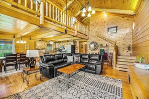 A spacious living area with a black leather sofa, wooden coffee table, and a patterned rug. A staircase leads to an upper level with a wooden railing. - Waterwheel Retreat - Classic Home • Hot Tub & Cozy Loft (Sturgis)