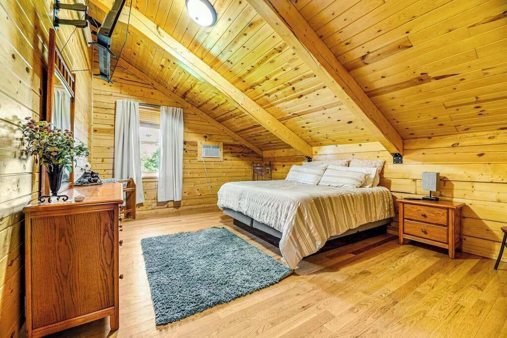 A cozy wooden cabin bedroom with a bed, bedside tables, a dresser, and a window with curtains.