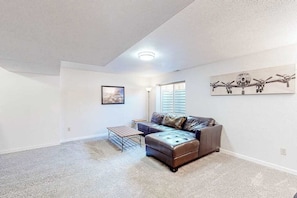 A living room with a sectional sofa, a coffee table, and a painting on the wall. - Windy Hill Retreat - Dog-Friendly Home • Huge Fenced Yard (Colorado Springs)