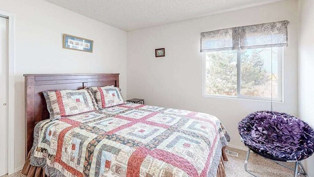 Quarto com cama de madeira, janela com vista e uma cadeira.
