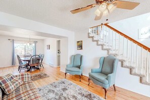 A spacious living room with a wooden floor, a staircase with a white railing, and two upholstered chairs. - Windy Hill Retreat - Dog-Friendly Home • Huge Fenced Yard (Colorado Springs)