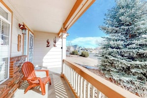 A porch with a wooden railing, a brick wall, and a red Adirondack chair. - Windy Hill Retreat - Dog-Friendly Home • Huge Fenced Yard (Colorado Springs)