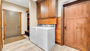 A laundry room with two front-loading washing machines, wooden cabinets, and a large wooden door. - Whiskey Ridge Lodge • Hot Tub & Rec Room (Sturgis)