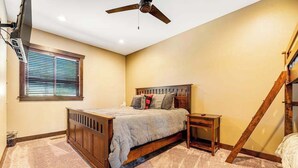 A bedroom with a bed, a nightstand, a ceiling fan, a window with blinds, and a staircase. - Whiskey Ridge Lodge • Hot Tub & Rec Room (Sturgis)