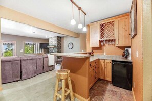 A kitchen with a bar area, wooden cabinets, a stone accent wall, and a black dishwasher. - Ridgeview Retreat - 3-Story Home • Private Hot Tub (Sturgis)