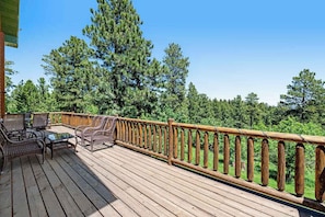 Eine Holzterrasse mit Gartenmöbeln und Geländer mit Blick auf einen Wald.