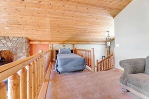 A bedroom with a wooden ceiling, a bed, a sofa, and a stone wall. - Ridgeview Retreat - 3-Story Home • Private Hot Tub (Sturgis)