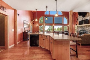 A spacious kitchen with a large island, wooden cabinets, and a stone fireplace. - Ridgeview Retreat - 3-Story Home • Private Hot Tub (Sturgis)