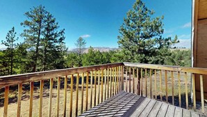 A wooden deck leading to a building with a view of trees and mountains.