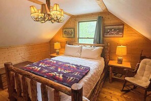 Ein gemütliches Schlafzimmer im Dachgeschoss mit einem großen Bett, einem Holz-Kopfstück, zwei Nachttischlampen, einem Schaukelstuhl und einem Fenster mit Blick.