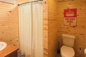 Ein Badezimmer einer Holzhütte mit Duschvorhang, Toilette und einem Schild, das einen Ausladerbereich kennzeichnet.