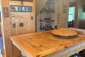 Ein Holzinterieur mit einem großen Tisch, einem an der Wand befestigten Regal mit Küchenutensilien und einer Tür mit Griff.