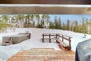 Eine Holzterrasse mit Whirlpool und Bänken mit Blick auf eine verschneite Landschaft mit Bäumen.