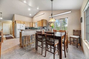 A kitchen with wooden cabinets, a dining table with chairs, and a pendant light. - Cliffview Cabin - ATV-Ready Cabin • Perfect Location (Nemo)