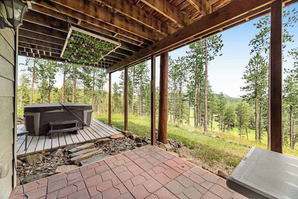 An outdoor deck with a hot tub, wooden beams, and a view of a forest.