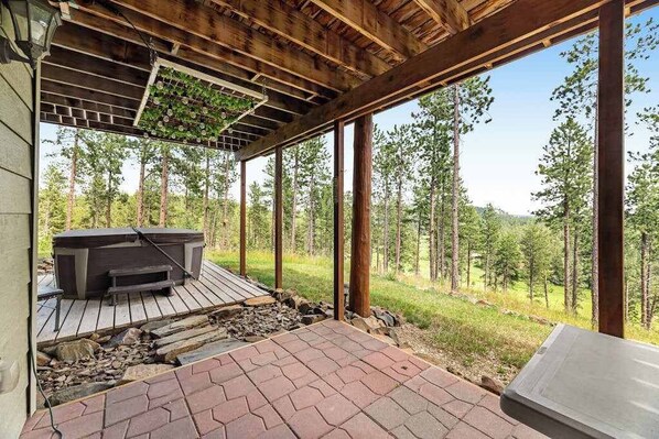 An outdoor deck with a hot tub, wooden beams, and a view of a forest. - Cliffview Cabin - ATV-Ready Cabin • Perfect Location (Nemo)