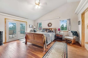 A bedroom with a wooden bed, a nightstand, a chair, a window with a view, and a sliding glass door leading to an outdoor area.