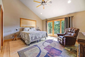 A bedroom with a bed, a chair, a desk, a ceiling fan, and a large window. - Eagle Crest Nest - Secluded Cabin • Hot Tub & Decks (Spearfish)
