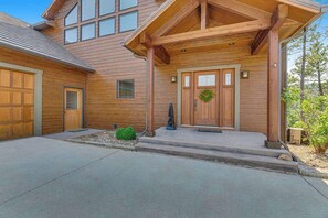A two-story wooden house with a covered porch, garage doors, and a small green bush. - Eagle Crest Nest - Secluded Cabin • Hot Tub & Decks (Spearfish)