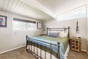 A bedroom with a metal bed frame, a window with blinds, a bedside table, and a wall-mounted lamp. - Goldfish Glen - Dog-Friendly Home • Pond & Mtn Views (Colorado Springs)