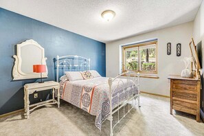 A bedroom with a bed, bedside table, lamp, dresser, and a window with a view. - 20-Acre Lodge • Hot Tub, Sauna • Dogs OK (Rapid City)