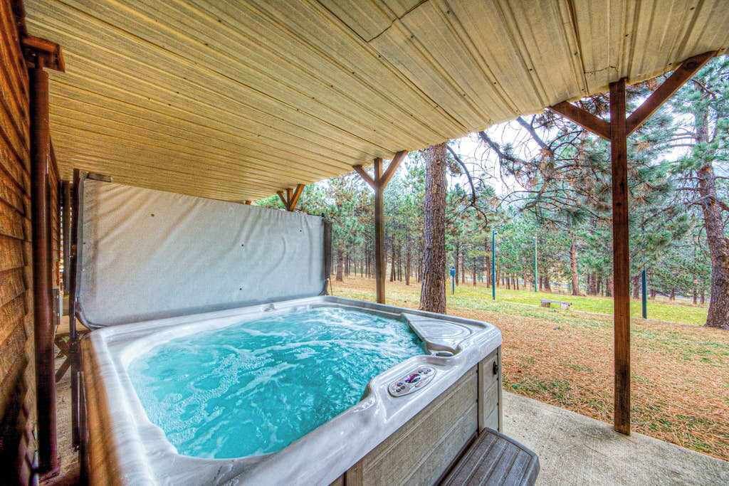 Un bain à remous sous une pergola en bois, avec vue sur une zone boisée.