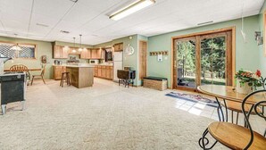 A spacious kitchen with wooden cabinets, a central island, and a dining area with a table and chairs. - Crooked Canyon Lodge - Secluded Lodge • Sauna & Hot Tub (Rapid City)