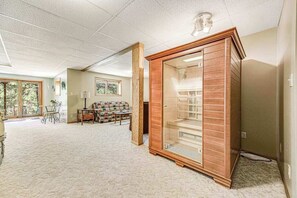 A spacious room with a large window, a wooden cabinet, and a carpeted floor. - Crooked Canyon Lodge - Secluded Lodge • Sauna & Hot Tub (Rapid City)