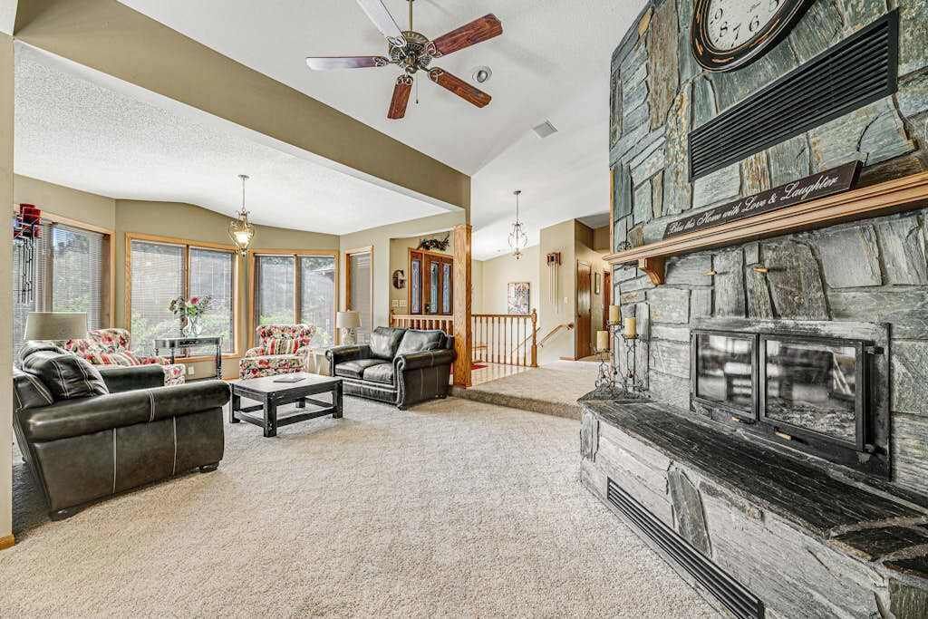 A spacious living room with a fireplace, leather sofas, and a ceiling fan.