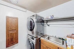 A laundry area with a washing machine, a dryer, and a wooden cabinet. - Hill City Haven • Black Hills Views & Deck (Hill City)