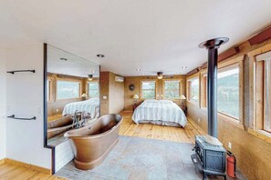 Une chambre à coucher avec un grand lit, une baignoire, une cheminée et un miroir qui reflète la pièce.