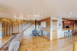 Un vaste espace de vie doté d’un plancher en bois, d’un canapé, d’un escalier et d’un coin cuisine avec des meubles en bois et un bar.
