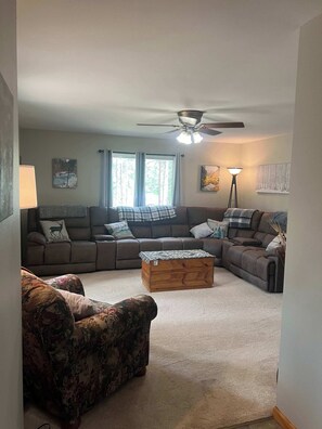 A living room with a sectional sofa, a wooden coffee table, and a patterned armchair. - Mountain Escape - Mountain-View Home + Cabin w/ Deck (Sturgis)