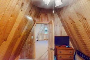 A wooden interior with a television on a dresser, a staircase leading to an upper level, and a ceiling light. - Mountain Escape - Mountain-View Home + Cabin w/ Deck (Sturgis)
