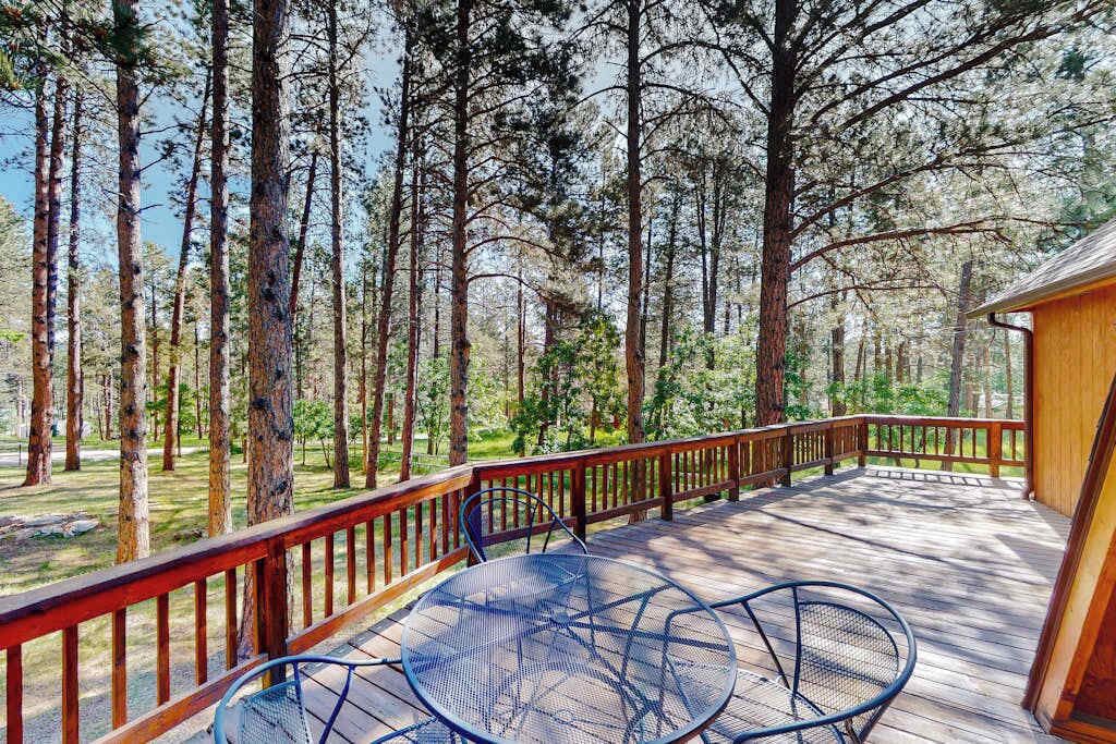 Eine Holzterrasse mit Metallstühlen und einem Tisch, umgeben von hohen Bäumen.