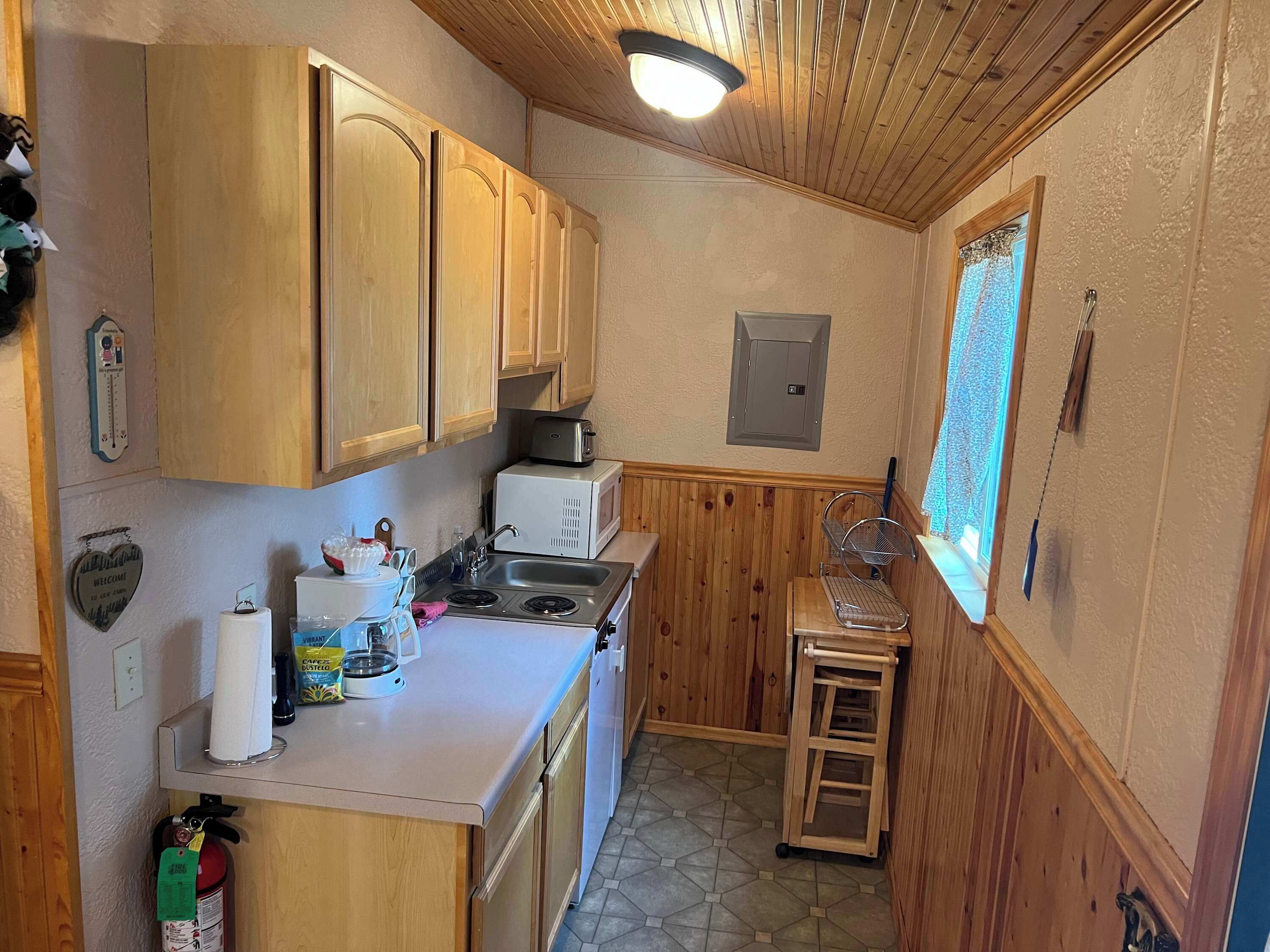 A compact kitchen with wooden cabinets, a microwave, a sink, and a small window.
