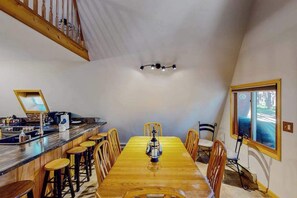 A dining area with a wooden table, bar stools, and a chandelier. - Mountain Escape - Mountain-View Home + Cabin w/ Deck (Sturgis)