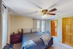 A bedroom with a bed, a nightstand, a chair, a ceiling fan, and a door leading to another room. - Mountain Escape - Mountain-View Home + Cabin w/ Deck (Sturgis)