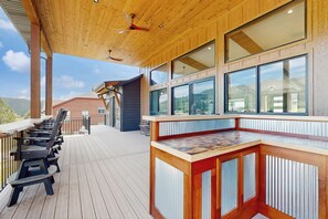 A wooden deck with outdoor seating and a bar area with large windows. - Eagles Nest on 17- Hot Tub Home • Lake Views & Game Room (Sturgis)