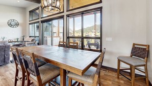 Un comedor con una gran mesa de madera, varias sillas y vistas amplias a través de grandes ventanales.
