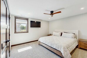 Une chambre à coucher comprenant un lit, une table de chevet, un ventilateur de plafond, une fenêtre et un téléviseur fixé au mur.