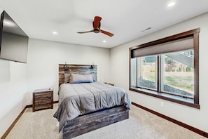 A bedroom with a bed, a nightstand, a ceiling fan, a window with a view, and a wooden headboard. - Eagles Nest on 17- Hot Tub Home • Lake Views & Game Room (Sturgis)