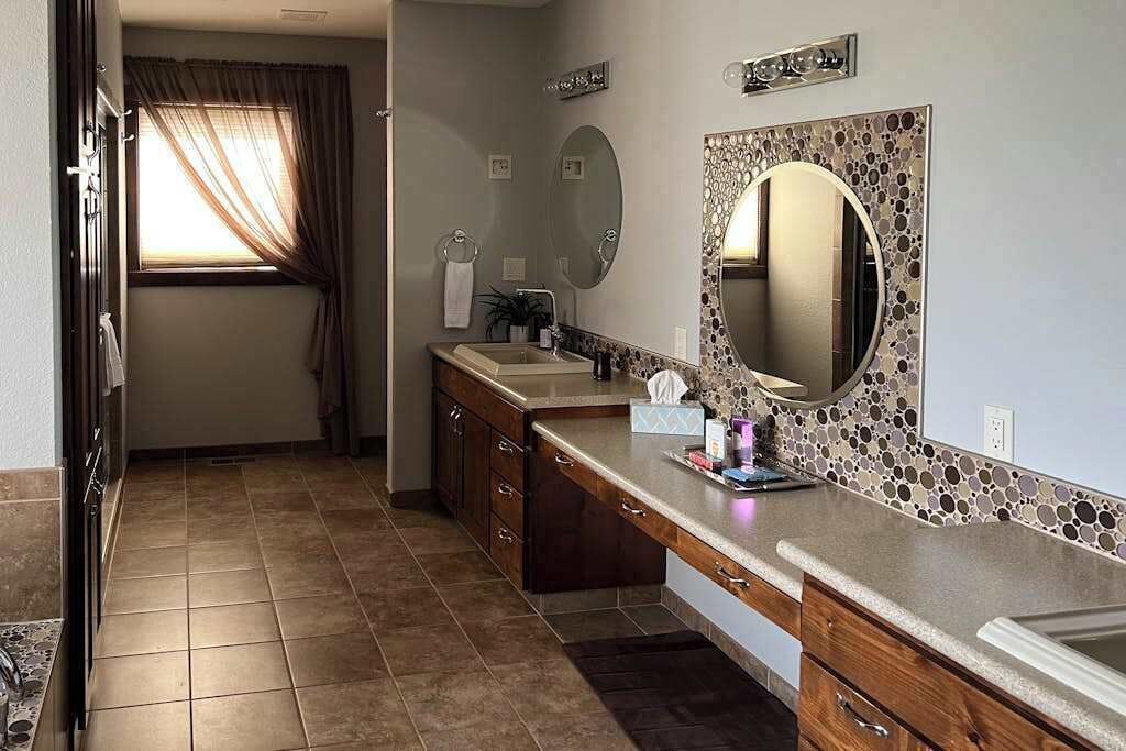 A bathroom with a vanity, a large mirror, and a window with curtains.