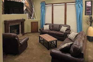 Ein Wohnzimmer mit Kamin, Ledersofas, einem Couchtisch und einem an der Wand montierten Fernseher.