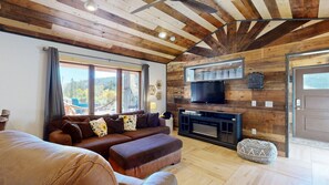 Ein gemütliches Wohnzimmer mit Holzbalkendecke, einer Sofagarnitur, einem Fernseher und einem Kamin.