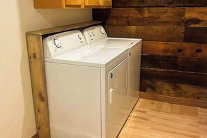 A white front-loading washer and dryer unit with a wooden panel wall and a wooden floor. - Honey Bee Hideaway- Dog-Friendly Home - Porch & Mtn Views (Lead)