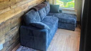 Huoneessa on puuseinä, sininen sohva ja ikkuna, josta avautuu näkymä vehreään maisemaan.