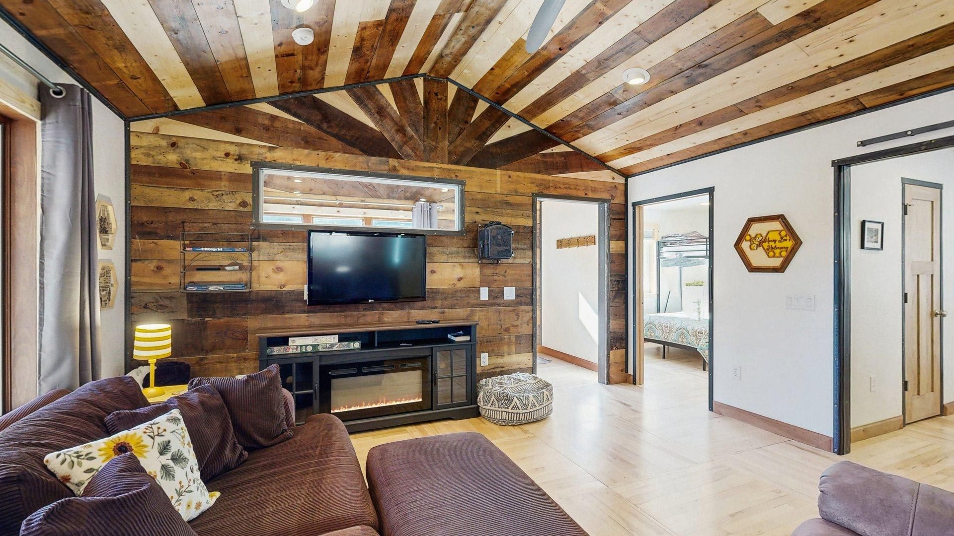 A modern living room with a wooden ceiling, a flat-screen TV mounted above a fireplace, and a sofa with cushions.